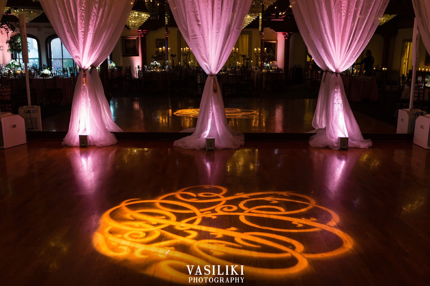 A monogram projected on the dance floor between draped columns