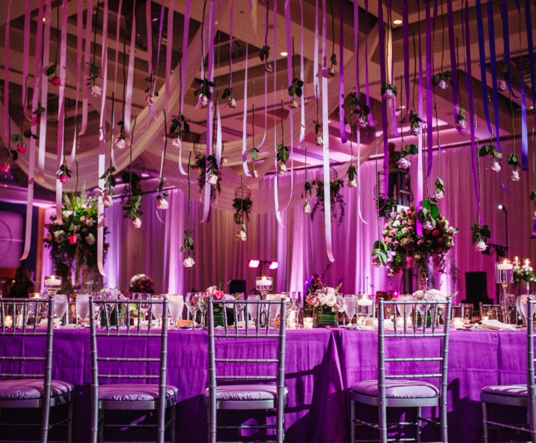 A ballroom dressed with hanging florals and violet uplighting